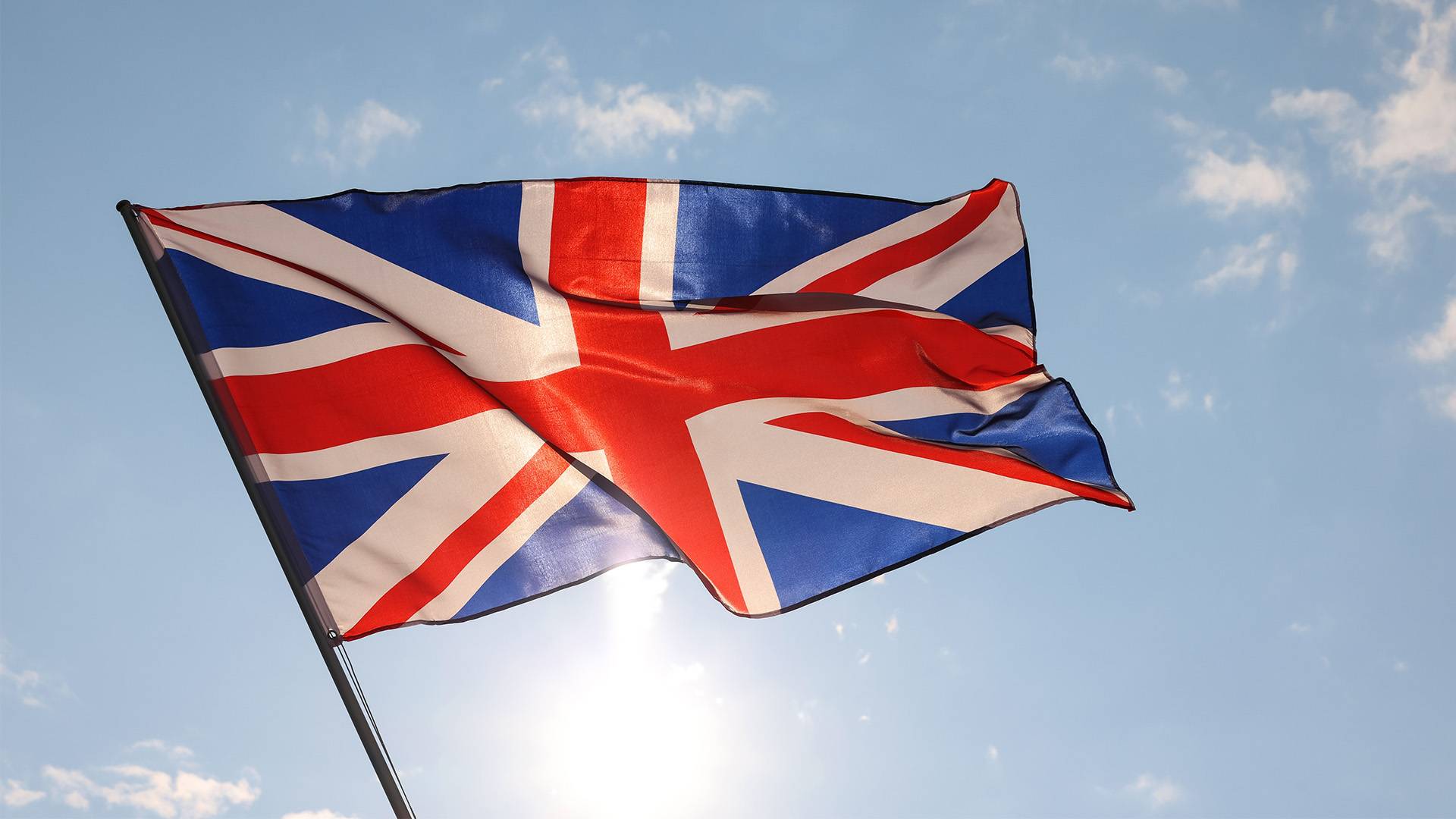 The Union Jack flag against a bright blue sky with clouds. 