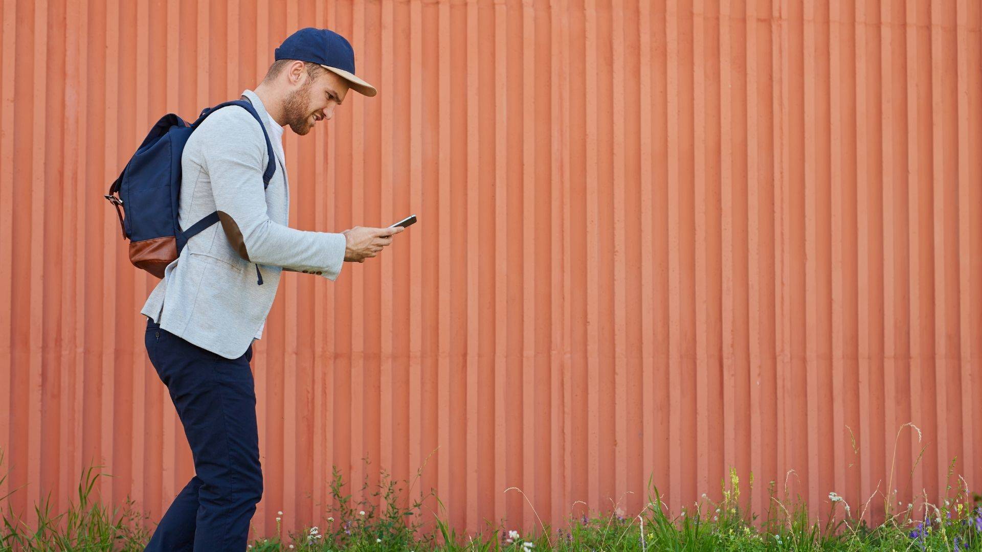 A gamer wearing a baseball cap, shirt and rucksack, playing an active mobile game.